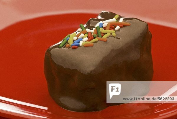 Brownie mit Schokoglasur und Zuckerstreuseln auf rotem Teller