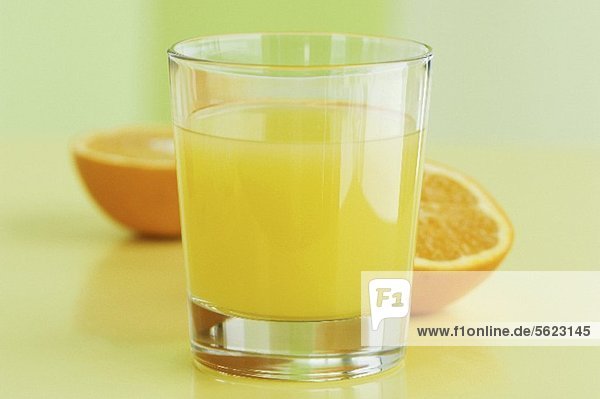 Ein Glas Orangensaft vor Orangenhälften