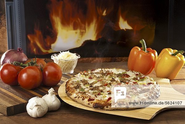 Pizza mit Hähnchen und Gemüse auf Pizzaschaufel vor Holzofen