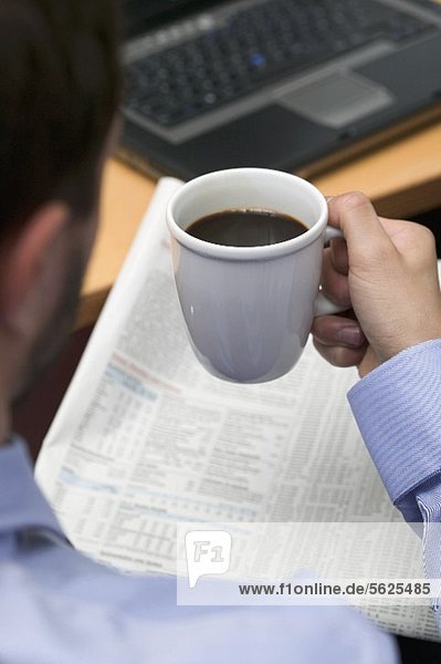 Geschäftsmann trinkt Kaffee beim Zeitunglesen im Büro