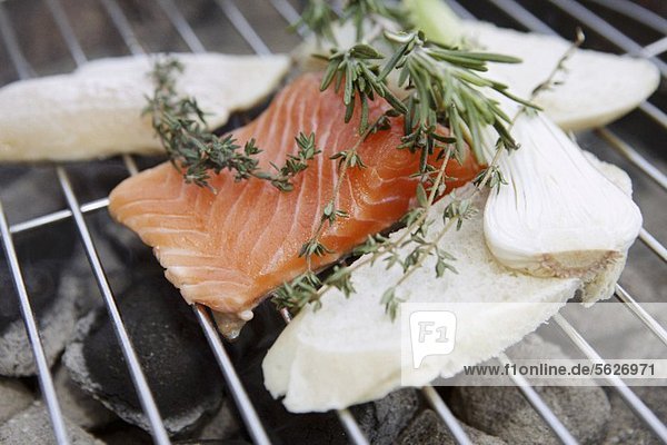A salmon fillet and slices of bread on a barbecue with bunches of herbs