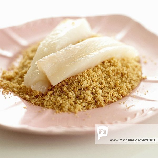 Raw fish fillets on a pile of breadcrumbs