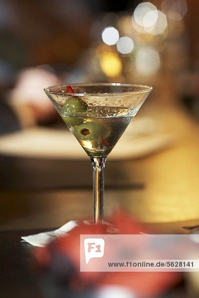Ein halb ausgetrunkener Martini mit grünen Oliven