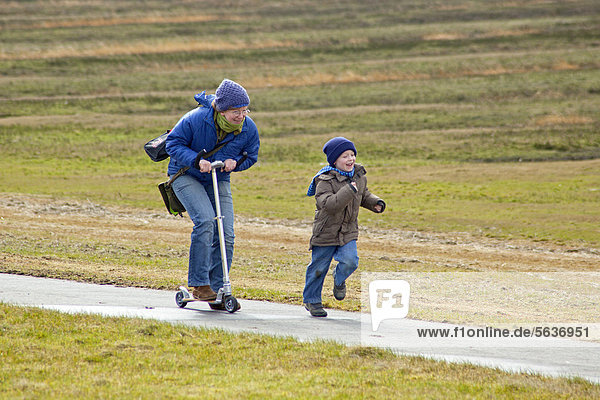 Race between a mother riding a scooter and her son running  Westerhever  Schleswig-Holstein  Germany  Europe
