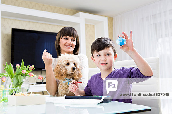 Young woman and her son  painting Easter egg  watched by a poodle
