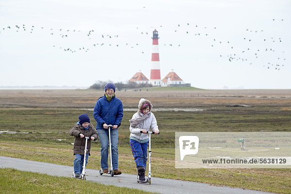 Mother and children riding kickboards  Westerhever Lighthouse  Schleswig-Holstein  Germany  Europe
