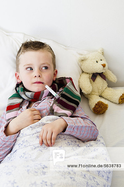 Junge mit Thermometer im Mund im Bett