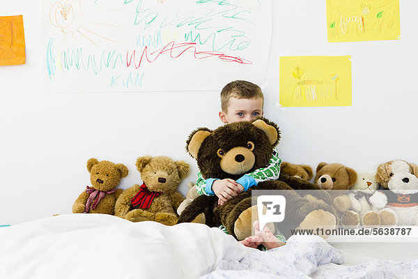 Junge umarmender Teddybär auf dem Bett