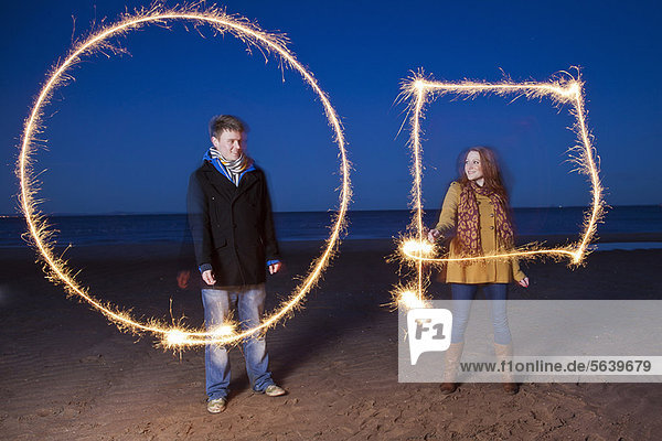 Couple playing with sparklers on beach