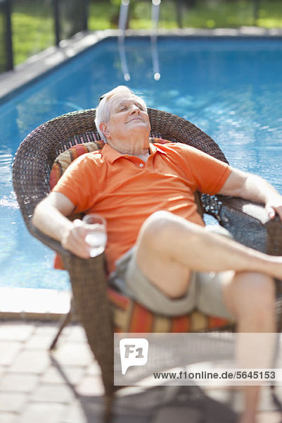 Ein pensionierter älterer Mann  der sich in der Sonne neben einem Pool entspannt.