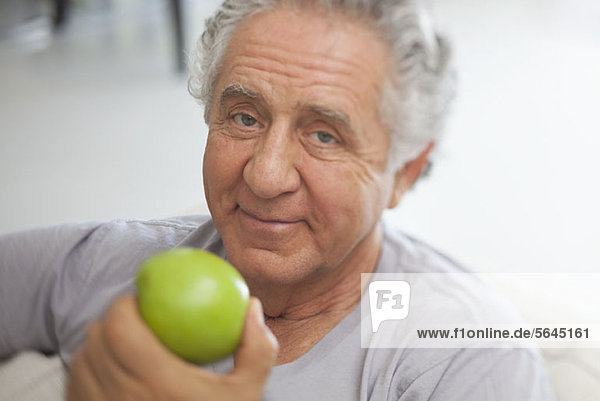Ein älterer Mann  der sich darauf vorbereitet  einen grünen Apfel zu essen.