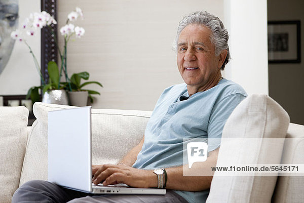 A cheerful senior man using a laptop at home