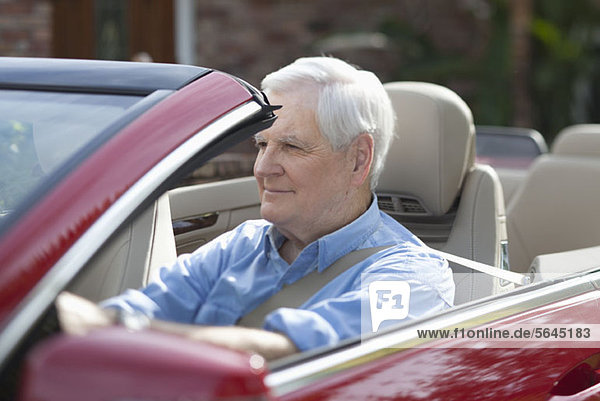 Ein älterer Mann  der einen Cabrio-Sportwagen fährt.