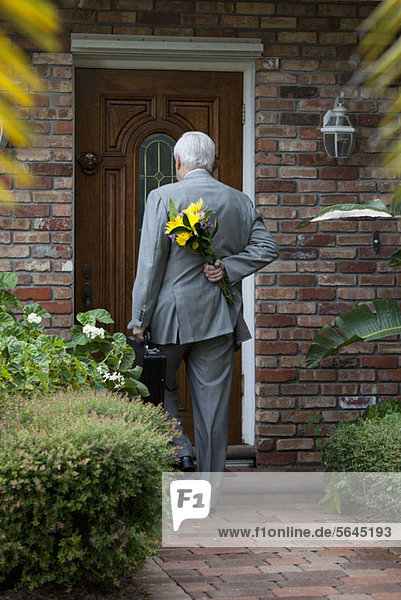 Ein Geschäftsmann mit Blumen hinter seinem Rücken  der nach Hause kommt.