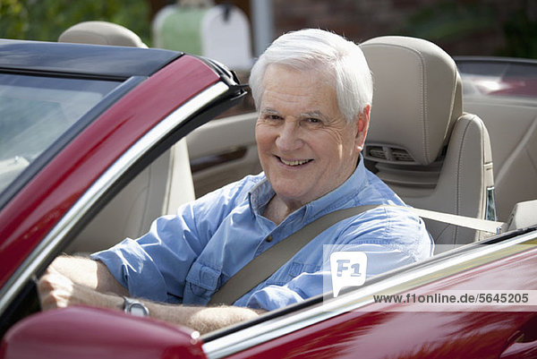 A cheerful senior man driving a convertible sports car