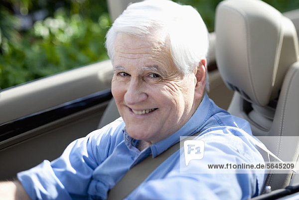 A cheerful senior man driving a convertible sports car