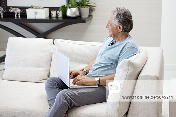 Ein älterer Mann  der einen Laptop in seinem Wohnzimmer benutzt.