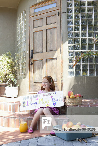 Mädchen verkauft Äpfel auf der Veranda und hält Zeichen