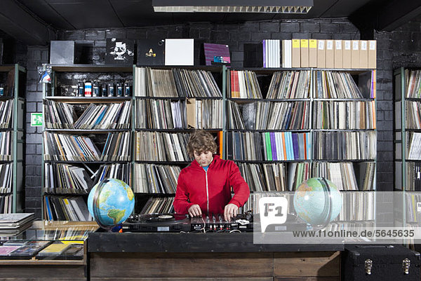 Ein junger Mann  der einen Soundmixer und DJ-Decks in einem Plattenladen benutzt.