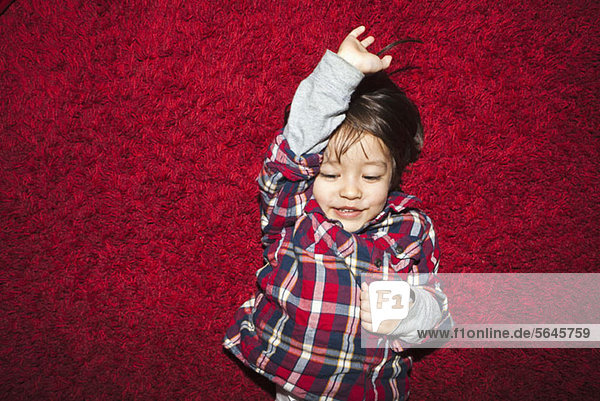 Ein junger lächelnder Junge liegt auf einem roten Teppich.