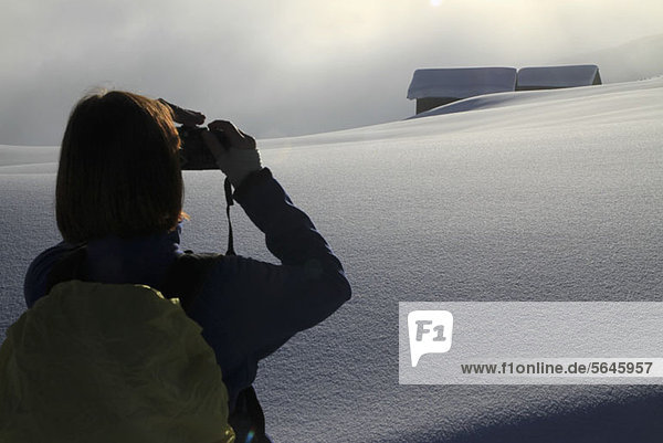 Wanderer fotografiert schneebedeckte Blockhütten in der Ferne