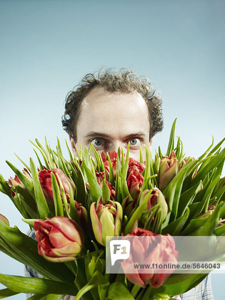 Ein Mann  der sich nervös hinter einem Strauß Tulpen versteckt.