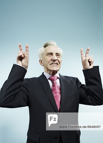 Ein älterer Mann mit erhobenen Händen macht Friedenszeichen.