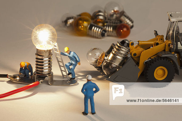 Miniatur-Elektrikerfiguren  die an einer beleuchteten Glühbirne arbeiten