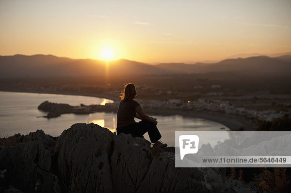 Eine Person mit Silhouette  die auf einem Hügel sitzt und den Sonnenuntergang beobachtet  Rhodos  Griechenland