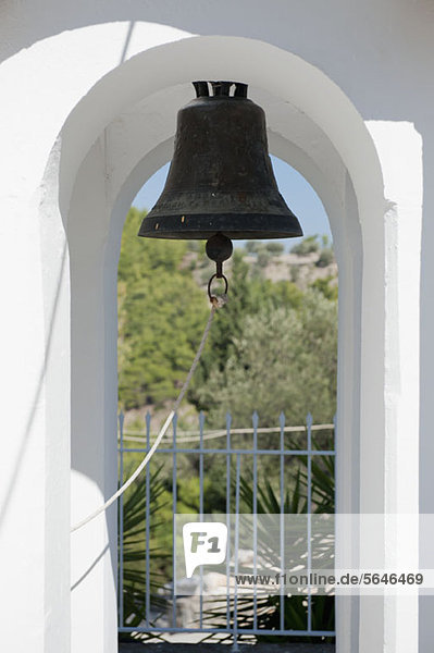 Eine altmodische Glocke  die in einem Torbogen hängt.