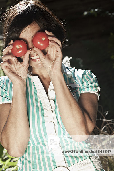 Austria  Salzburg  Flachau  Woman holding tomatoes in front of her eyes  smiling
