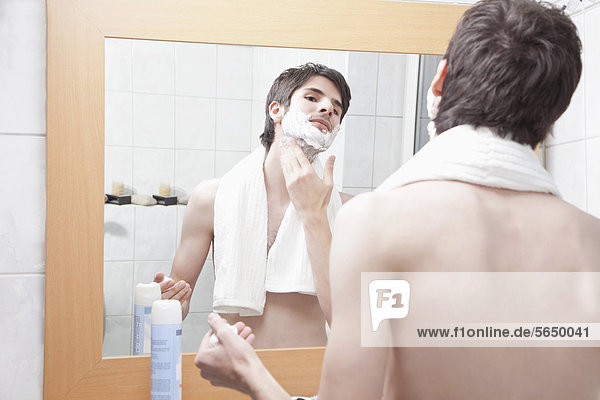 Junger Mann beim Auftragen von Rasiercreme im Bad