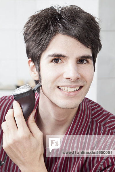 Junger Mann beim Rasieren mit Elektrorasierer  Portrait