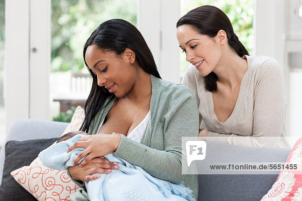 Young woman watching friend breastfeed her baby