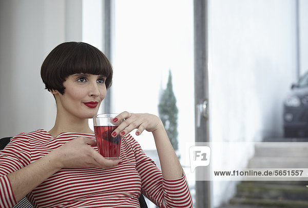 Junge Frau sitzend mit einem Glas Tee in der Wohnung