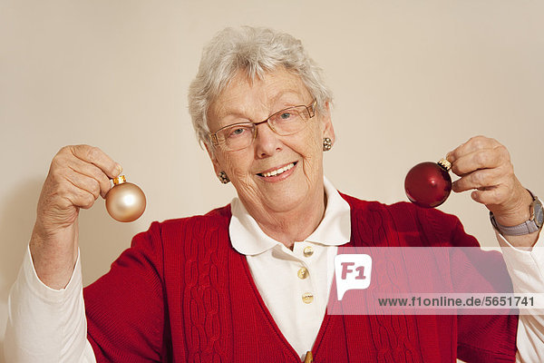 Senior woman holding christmas baubles  smiling  portrait