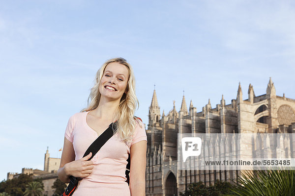 Spanien  Mallorca  Palma  Junge Frau stehend mit St. Maria Kathedrale im Hintergrund  lächelnd  Portrait
