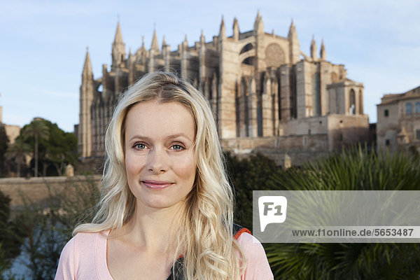 Spanien  Mallorca  Palma  Junge Frau stehend mit St. Maria Kathedrale im Hintergrund  lächelnd  Portrait
