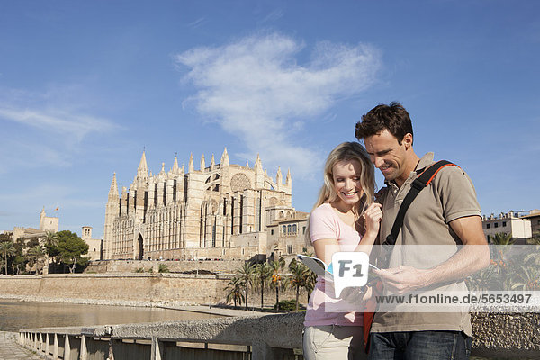 Spanien  Mallorca  Palma  Paar im Reiseführer mit der Kathedrale St. Maria im Hintergrund  lachend