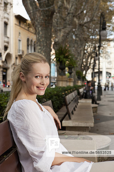 Spanien  Mallorca  Palma  Junge Frau auf Bank sitzend  lächelnd  Portrait