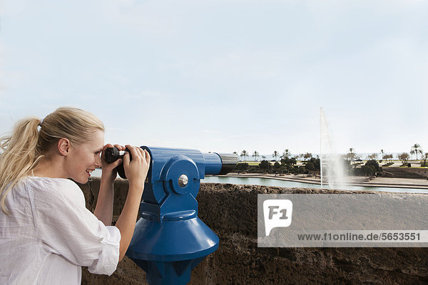 Spanien  Mallorca  Palma  Junge Frau schaut durchs Teleskop  lächelnd