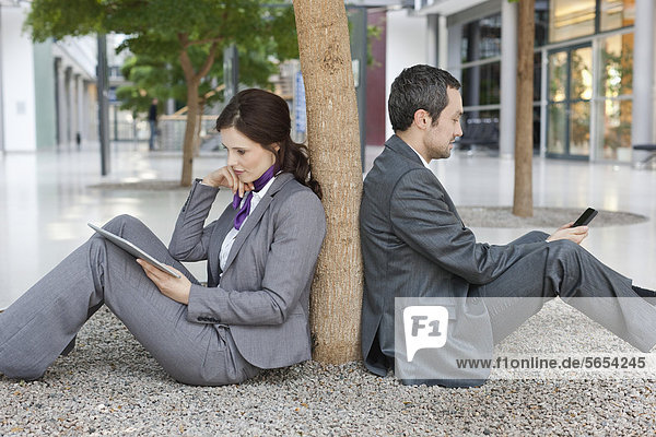 Deutschland  Leipzig  Geschäftsleute am Baum sitzend mit digitalem Tablett und Handy