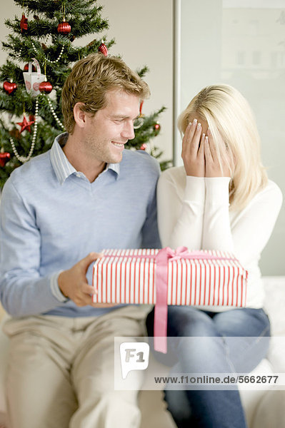 Junge Frau hält sich die Augen zu bekommt Weihnachtsgeschenk von ihrem Partner