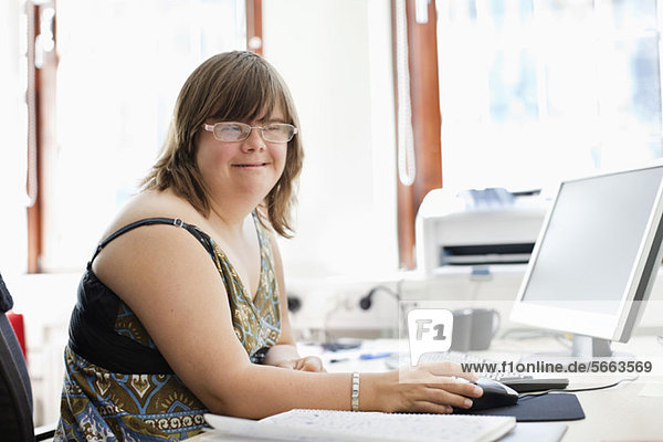 Porträt einer Frau mit Down-Syndrom am Computer im Büro