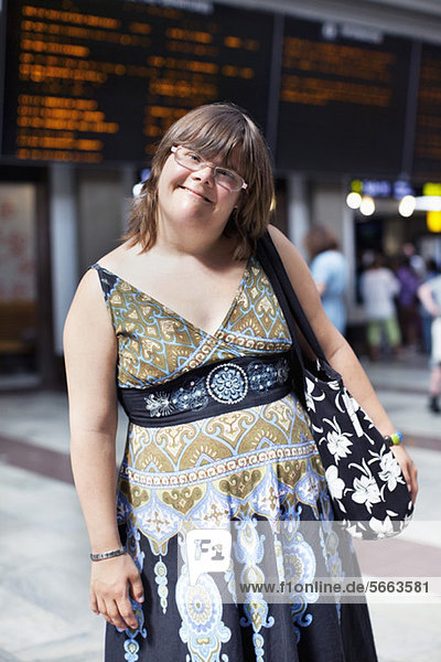 Porträt einer lächelnden Frau mit Down-Syndrom stehend mit Handtasche am Bahnhof