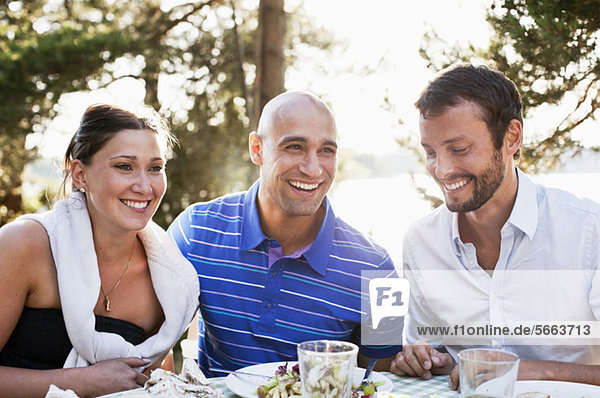 Drei Freunde  die beim Essen im Freien lächeln.