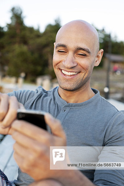 Mann lächelt  während Textnachrichten auf dem Handy gesendet werden