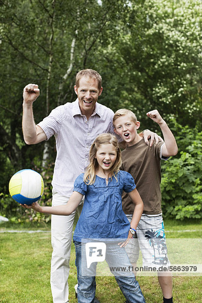 Portrait of excited father and children with soccer ball in back yard