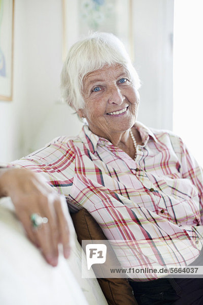 Porträt einer lächelnden Seniorin  die auf dem Sofa sitzt.