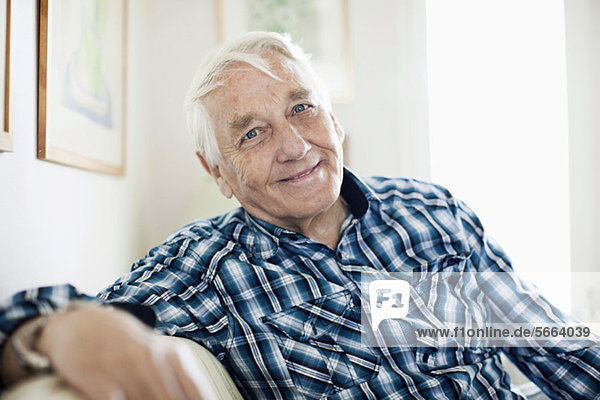 Porträt eines lächelnden älteren Mannes  der im Wohnzimmer sitzt.